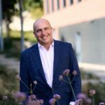 A cheerful man in a suit smiles amid urban greenery in Bratislava.